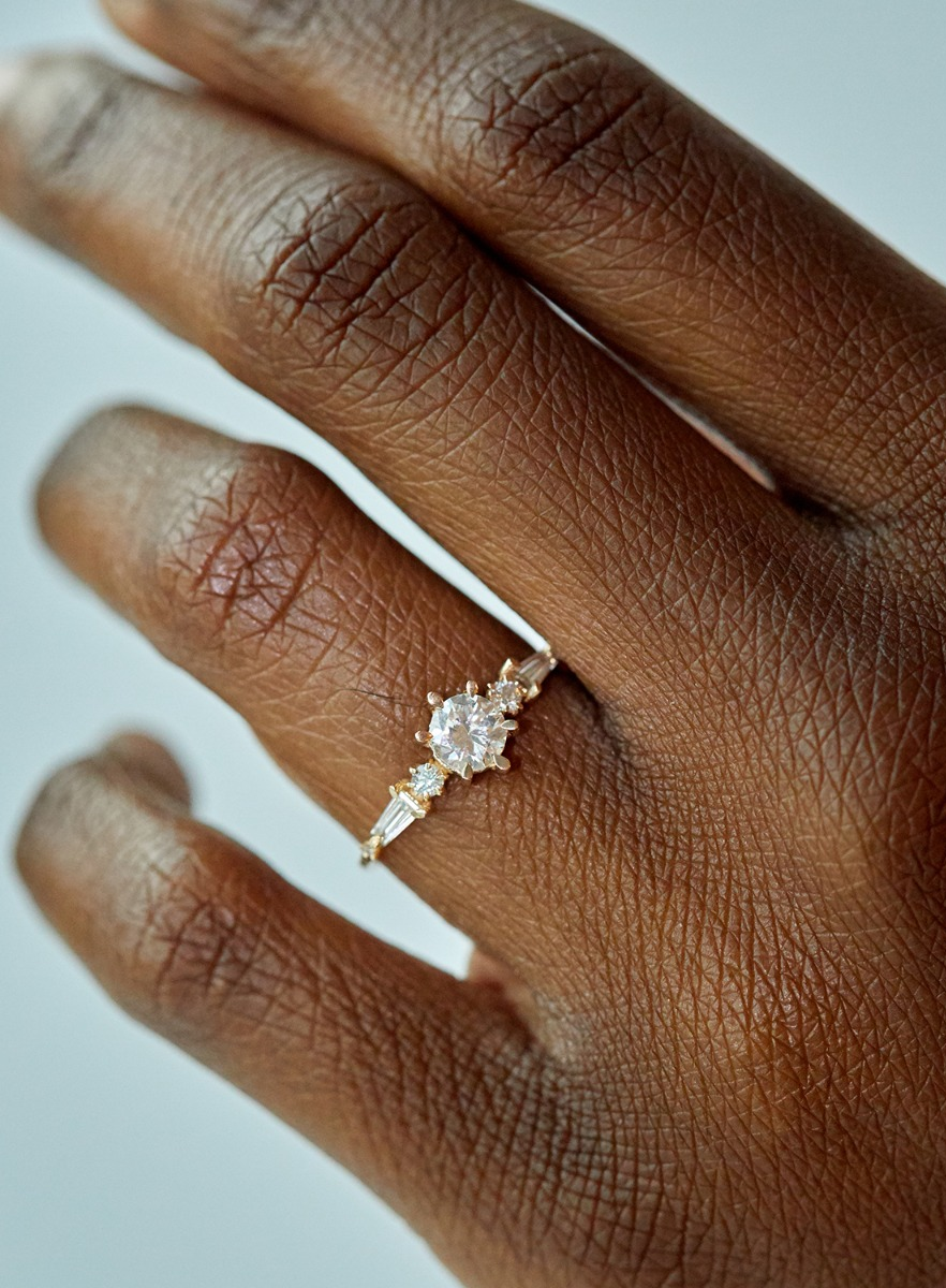 A close-up of a hand wearing a gold ring with a prominent diamond in a bright setting.