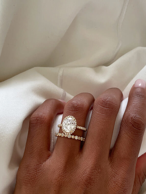 A hand model wearing a James Allen solitaire oval engagement ring and diamond pave wedding band.